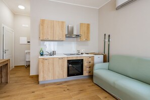 Una cucina compatta con mobili in legno, forno integrato e un divano verde chiaro in un appartamento moderno.