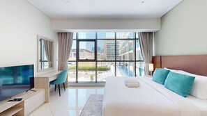 Ein Hotelzimmer mit Bett, Schreibtisch, Fernseher und großen Fenstern mit Blick auf die Stadt.