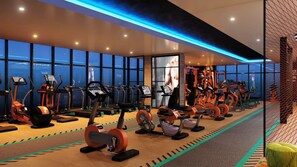 Ein Fitnessstudio mit verschiedenen Cardiogeräten, einem großen Bildschirm und Blick auf die Stadt durch große Fenster.