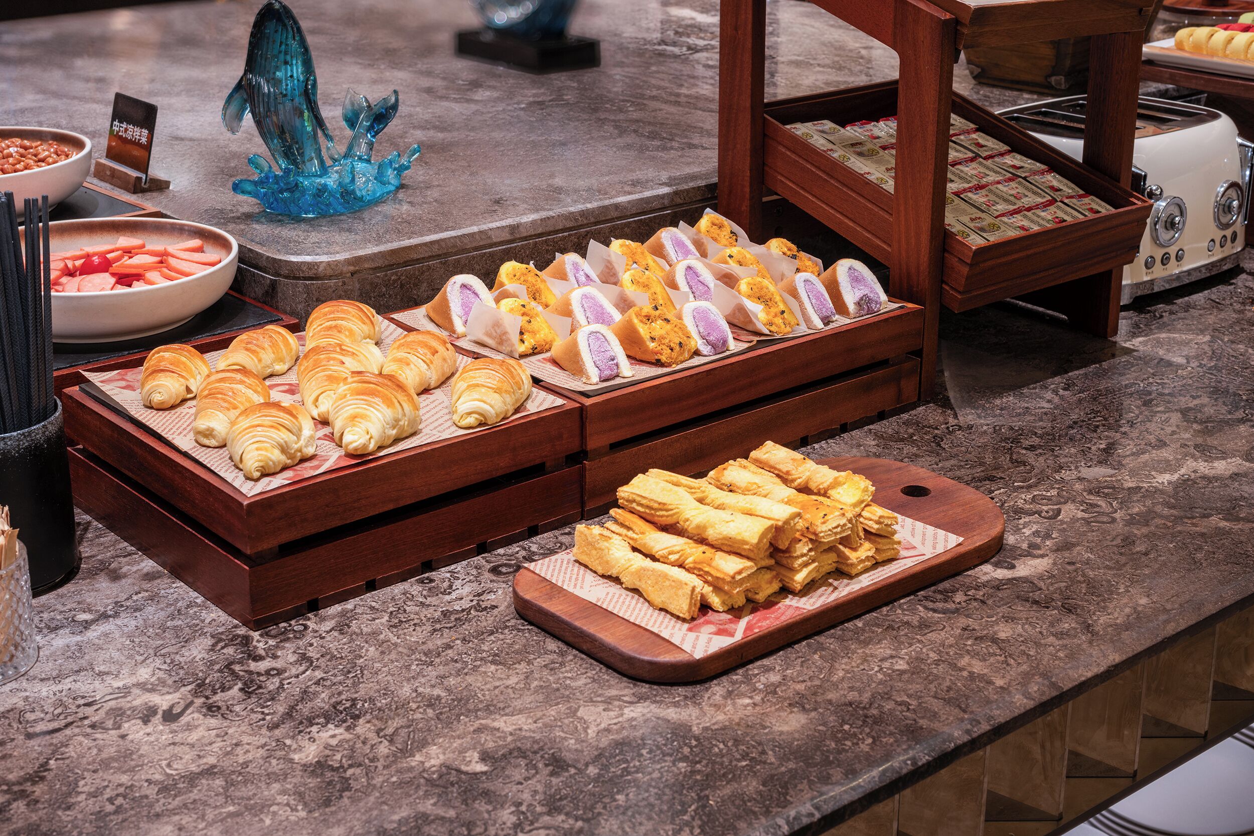 Un bufé con diversos productos de pastelería y una escultura decorativa de vidrio azul.