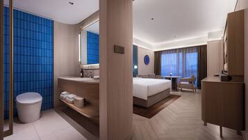 A modern hotel room with a large bed, a bathroom with a blue-tiled wall, a wooden vanity, and a large mirror.