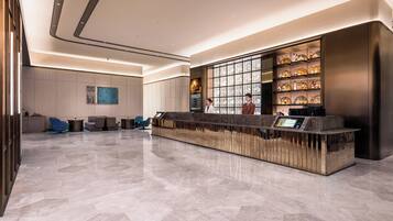 A modern hotel lobby with a reception desk, seating area, and a wall of decorative bottles.