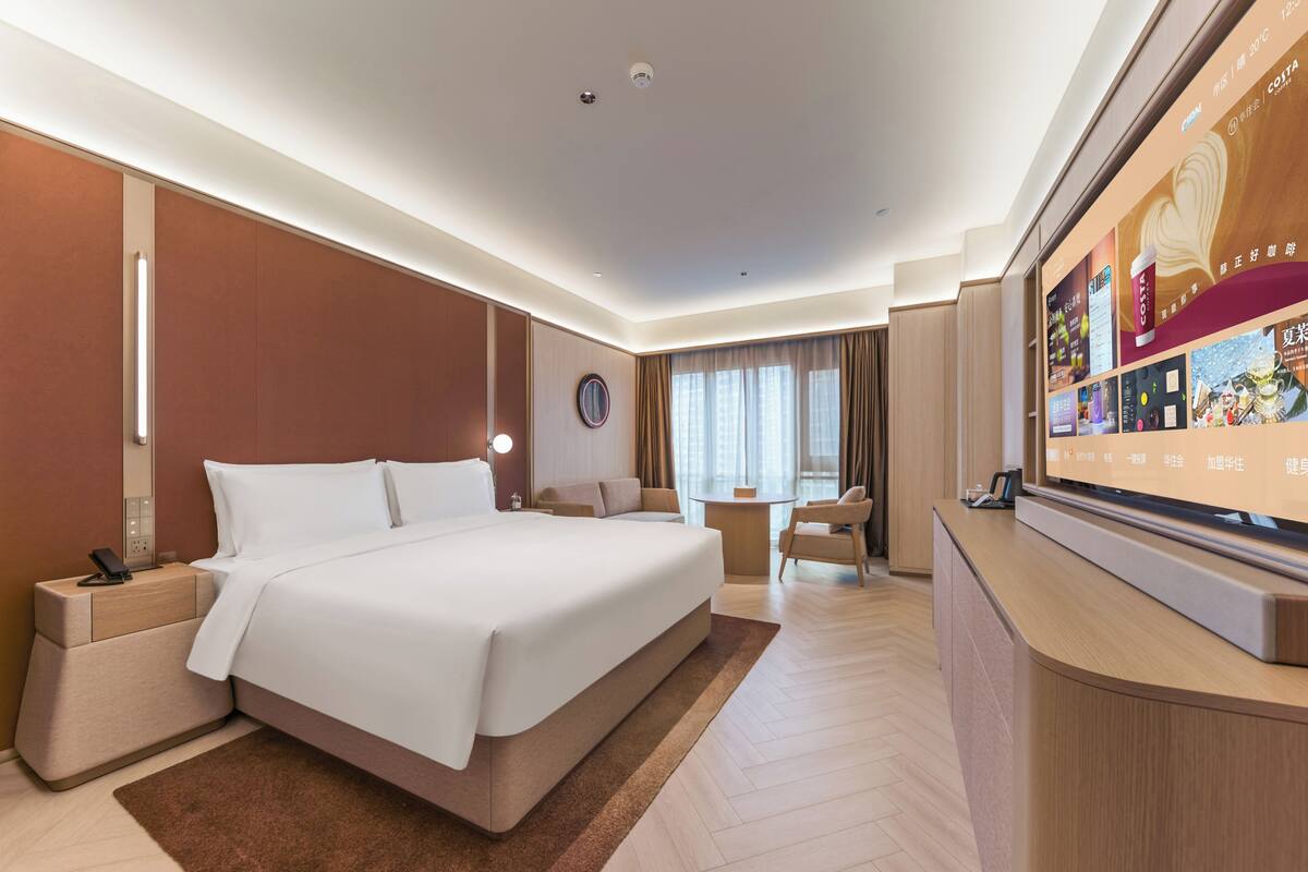 A hotel room with a large bed, bedside tables, a desk, a chair, and a television.