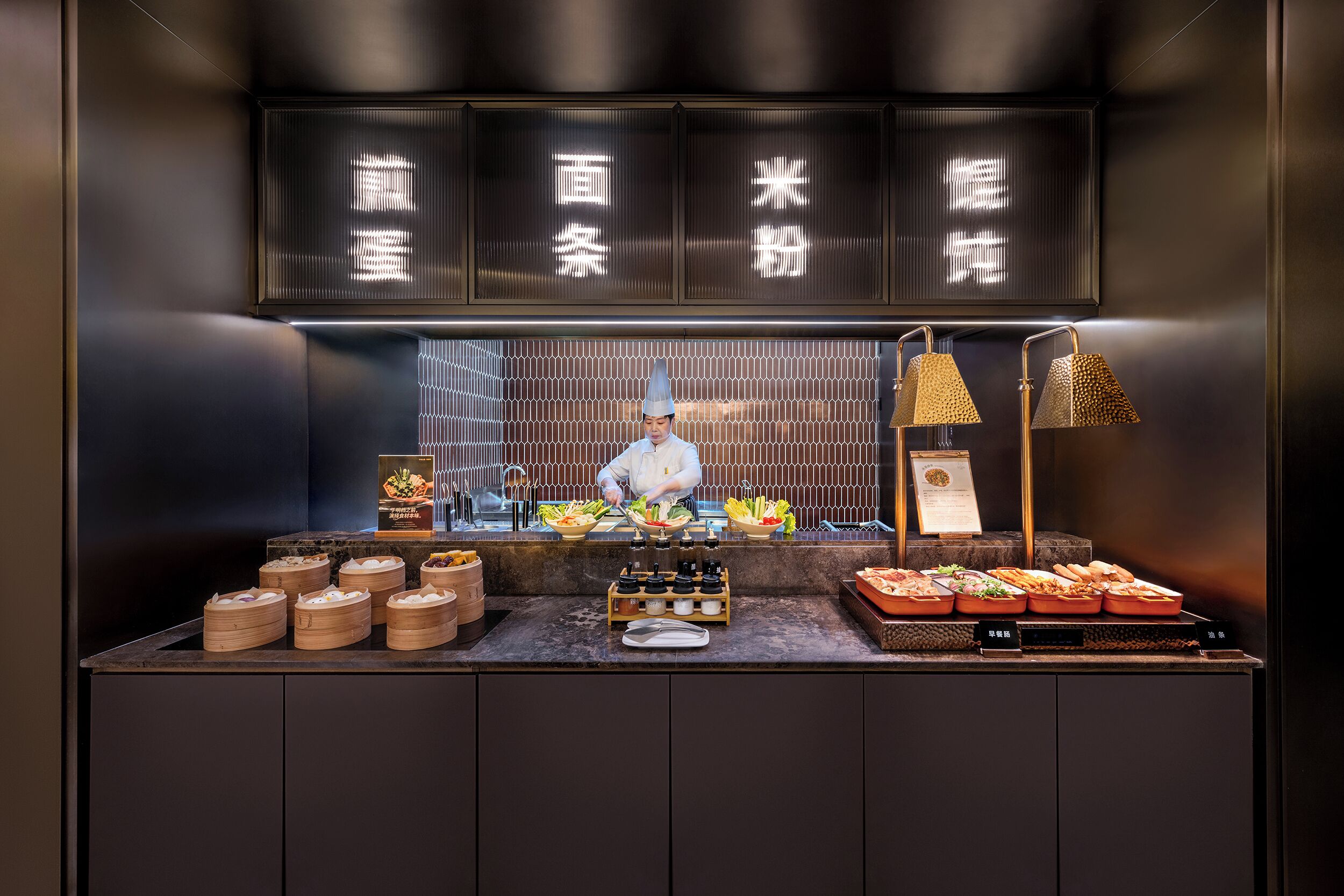 A chef preparing food in a modern kitchen with a display of various dishes and cooking utensils.