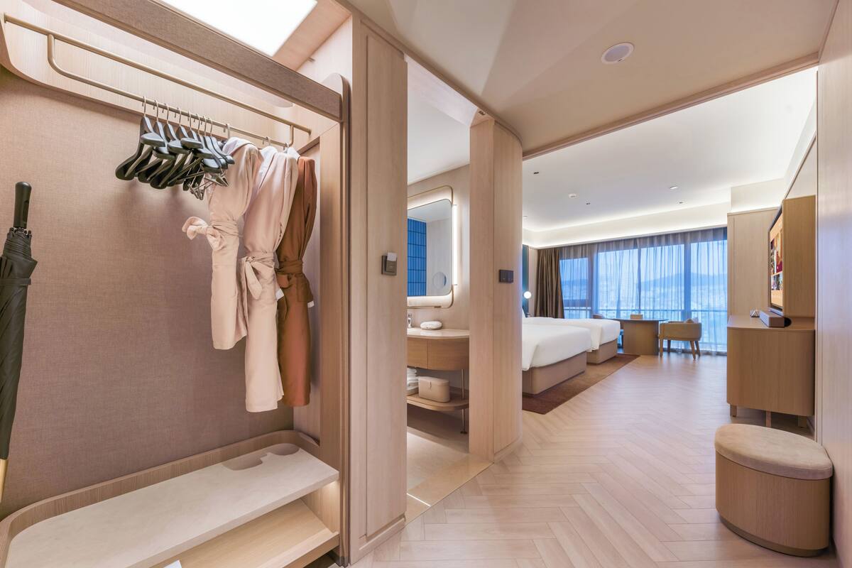 A modern hotel room with a large bed, a sitting area, a bathroom, and a view of the city.