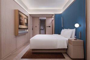 A modern hotel room with a large bed, a flat-screen TV, a bedside table with a lamp, and a blue accent wall. - Crystal Hotel Qingdao Taidong St. (Qingdao)