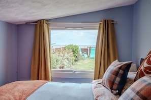 Ein Schlafzimmer mit Fenster, Vorhängen, einem Bett und Blick ins Freie.