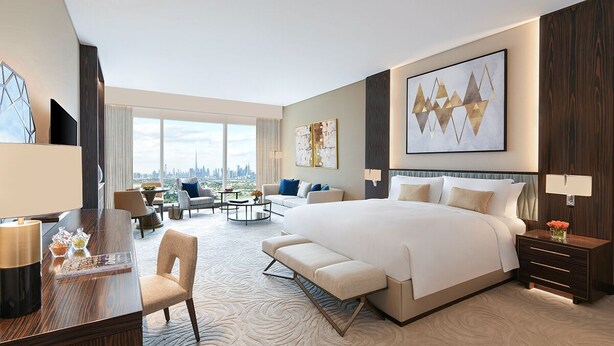 A modern hotel room with a large bed, a desk, a seating area, and a city view.