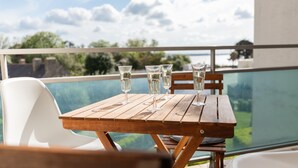 Een houten tafel met vier glaasjes op een balkon met uitzicht op een zwembad en groen.