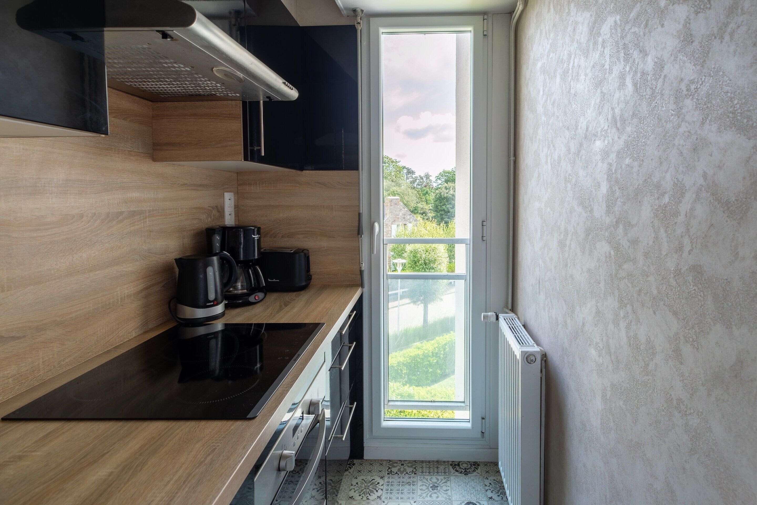 Une cuisine moderne avec un plan de travail noir, une machine à café et une vue sur la verdure à l’extérieur.