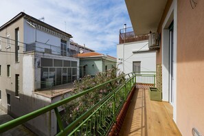 Un balcone con ringhiera verde, pavimento in legno e vista sui palazzi vicini.
