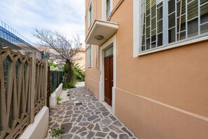 Un stretto sentiero in pietra conduce a un edificio con una porta in legno e una finestra con persiane.