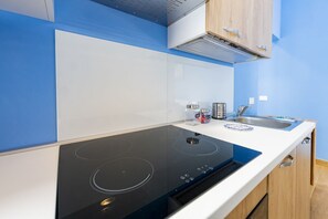 A modern kitchen with a black induction cooktop, a stainless steel sink, and wooden cabinets. - GuestHost - Cozy Balcony Apartment for 2 near the Sea (Francavilla al Mare)