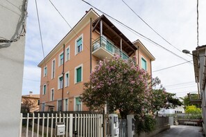 Un edificio a più piani con balconi, un ingresso carrabile e un albero con fiori rosa.