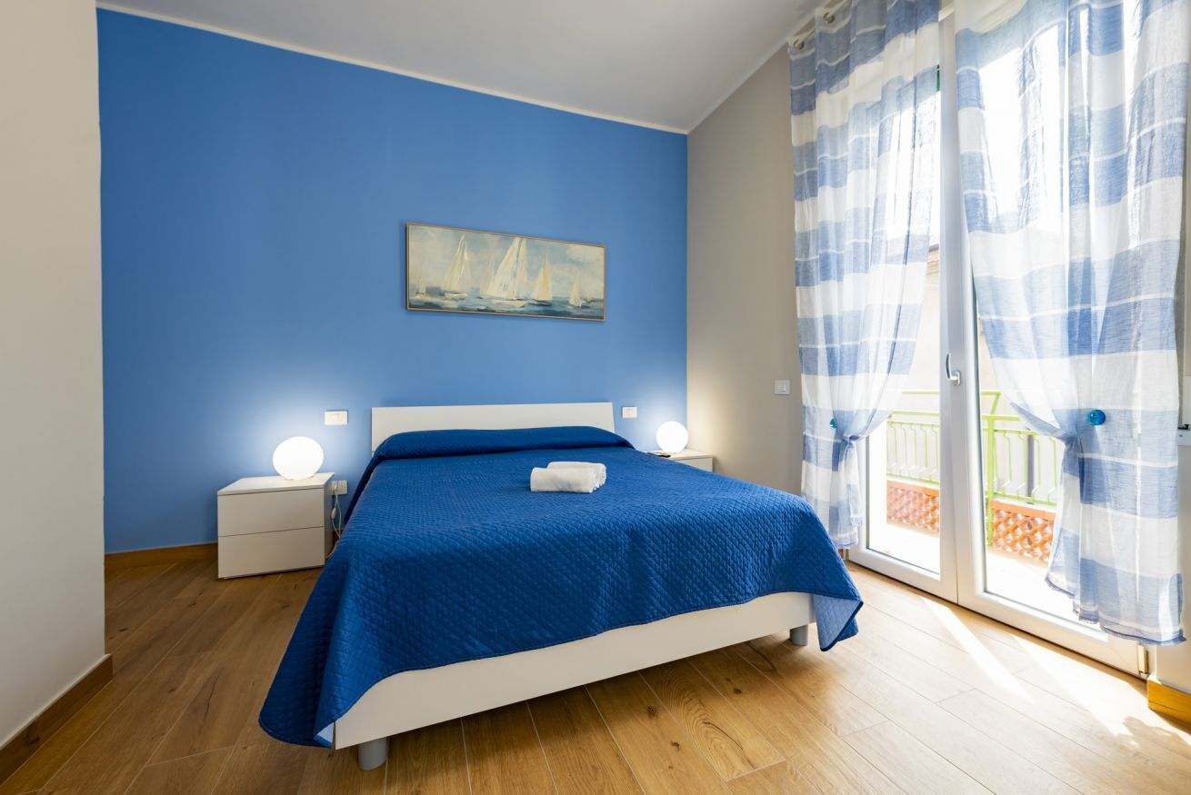 A bedroom with a bed, a nightstand, a wall-mounted lamp, and a painting.