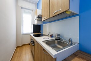 Una cucina compatta con mobili in legno, un lavello in acciaio inossidabile, un forno a microonde nero e una finestra.