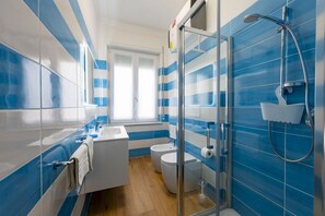Un bagno con piastrelle blu e bianche, box doccia in vetro, lavandino bianco e due servizi igienici.