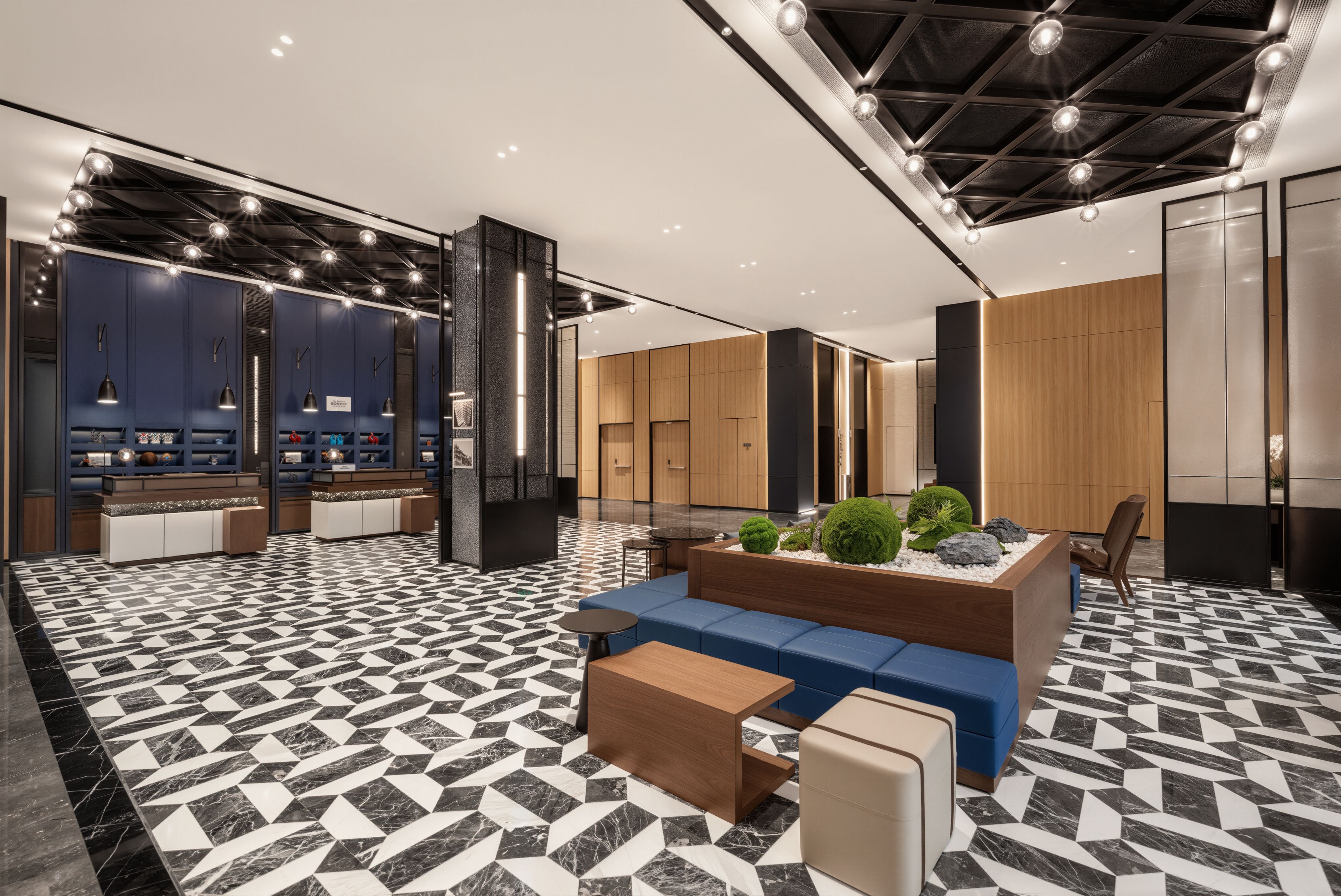 A modern hotel lobby with a geometric patterned floor, seating areas, and a reception desk.