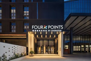 Entrada de un hotel con un cartel que dice 'FOUR POINTS BY SHERATON' y una fachada de edificio moderna al fondo.
