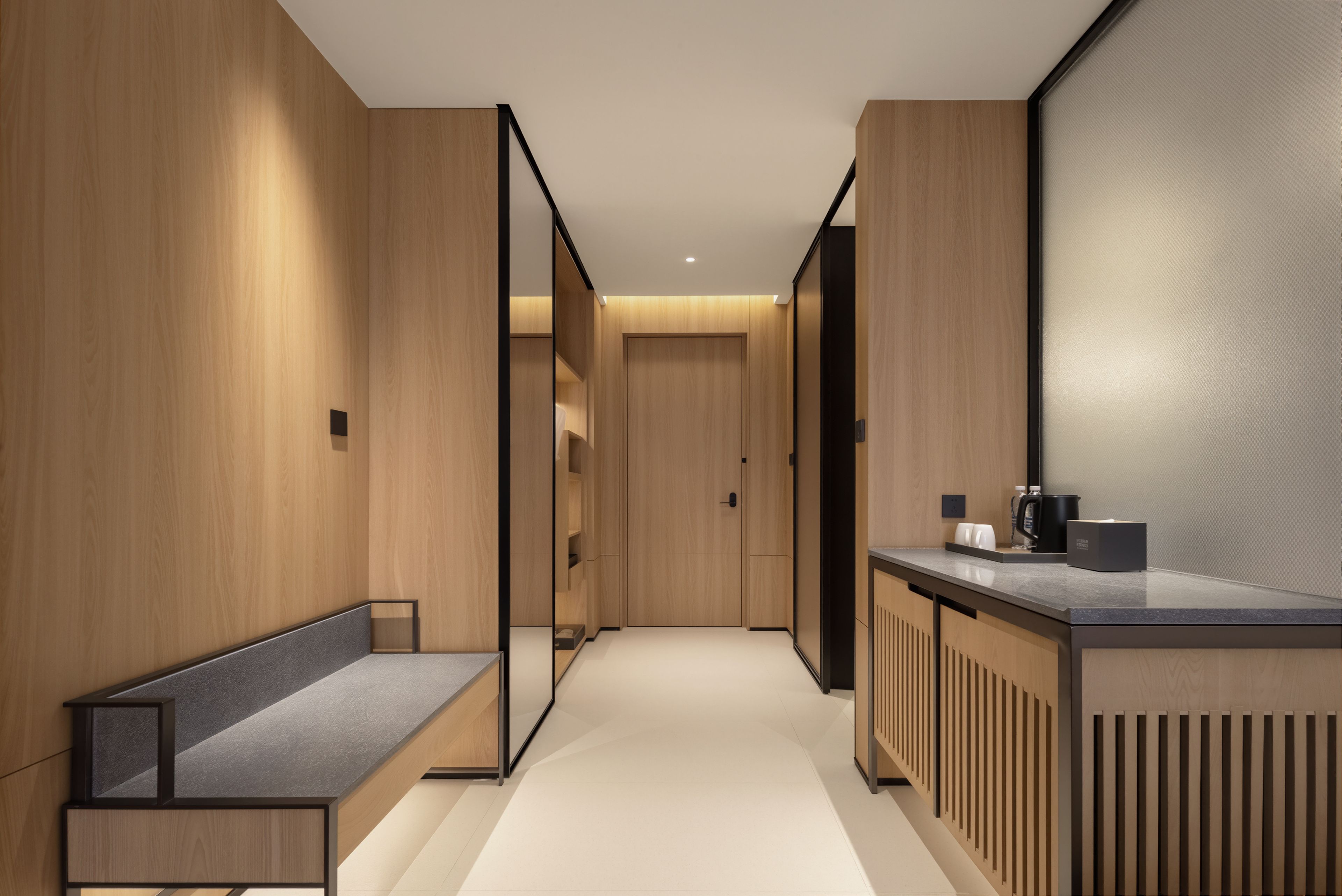 A modern hallway with wooden walls, a bench, a counter with a coffee machine, and a large mirror.