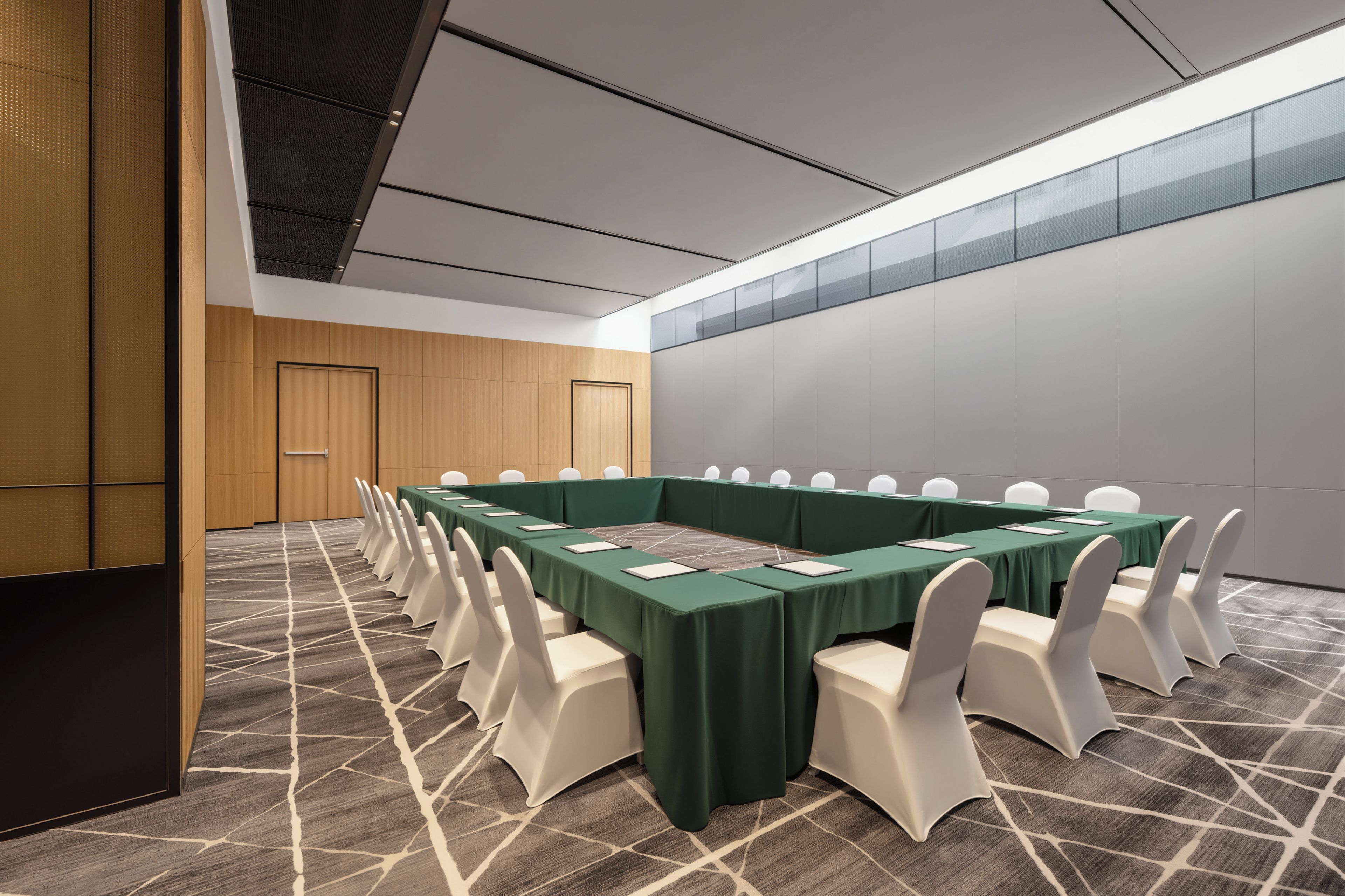 A conference room with a long table, white chairs, and a green tablecloth.