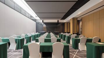 A conference room with rows of tables and chairs, a modern ceiling design, and a view of the adjacent room.