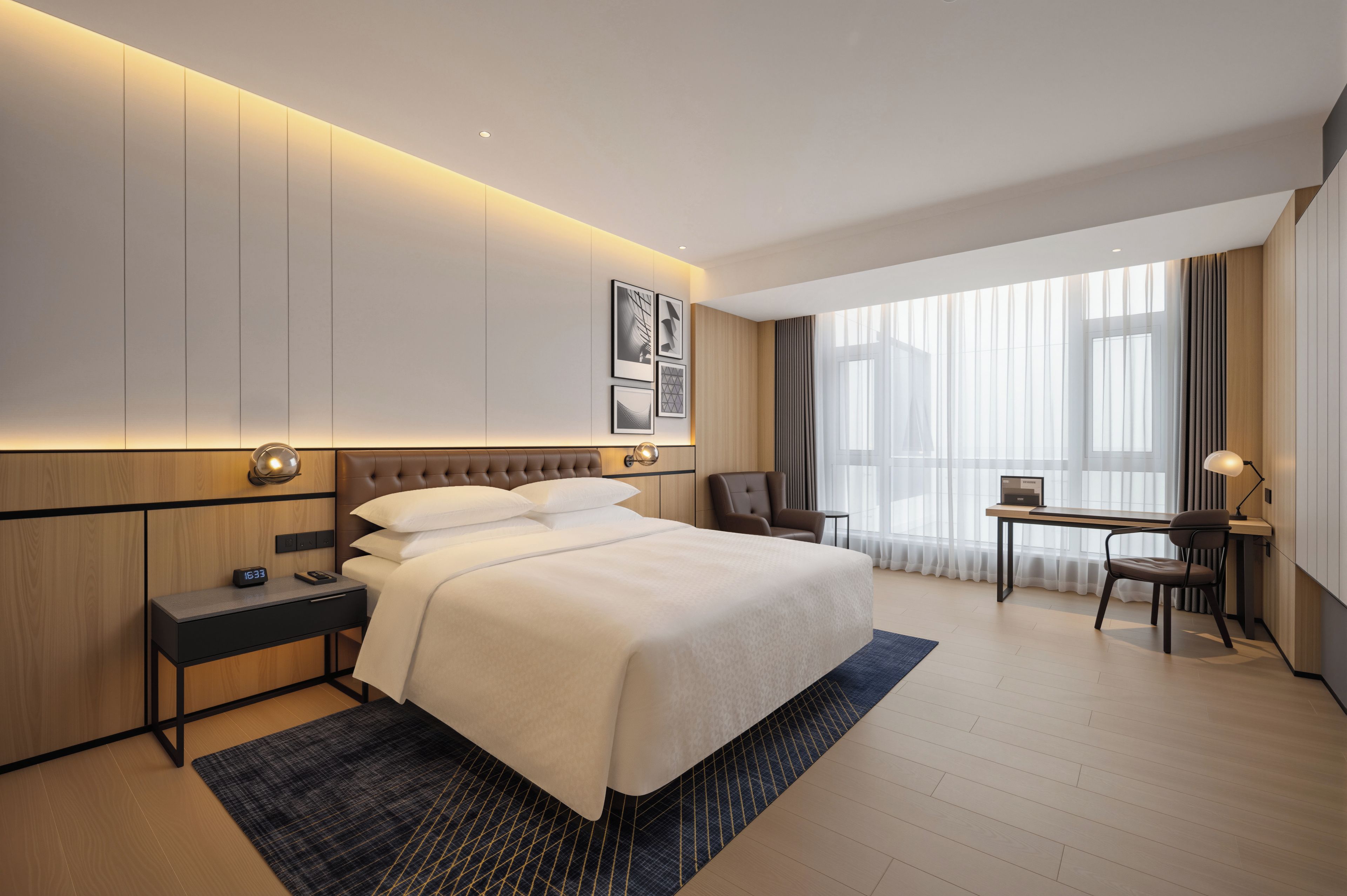 A hotel room with a bed, bedside table, desk, chair, and large windows.
