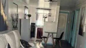 Ein modernes Wohnzimmer mit einem weißen Sofa, einem Glastisch und einem blau gemusterten Teppich.