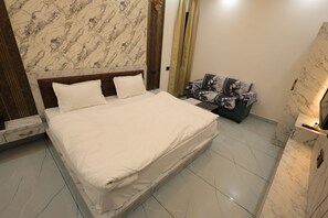 A hotel room with a large bed, marble-patterned walls, a nightstand, and a seating area with a patterned sofa. - Hotel Vinayak Vista (Khatoo)