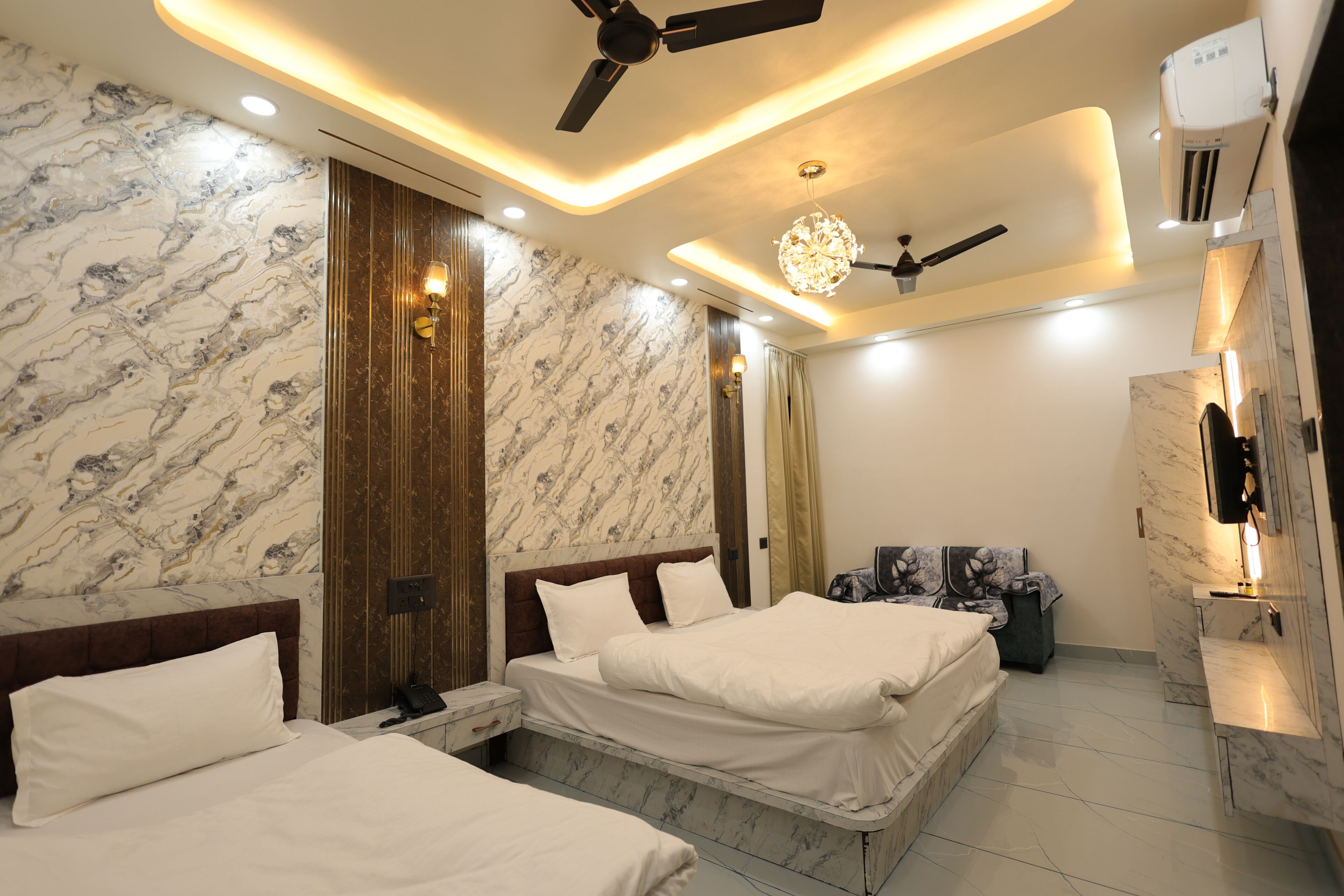 A hotel room with two beds, a ceiling fan, a chandelier, and marble walls.