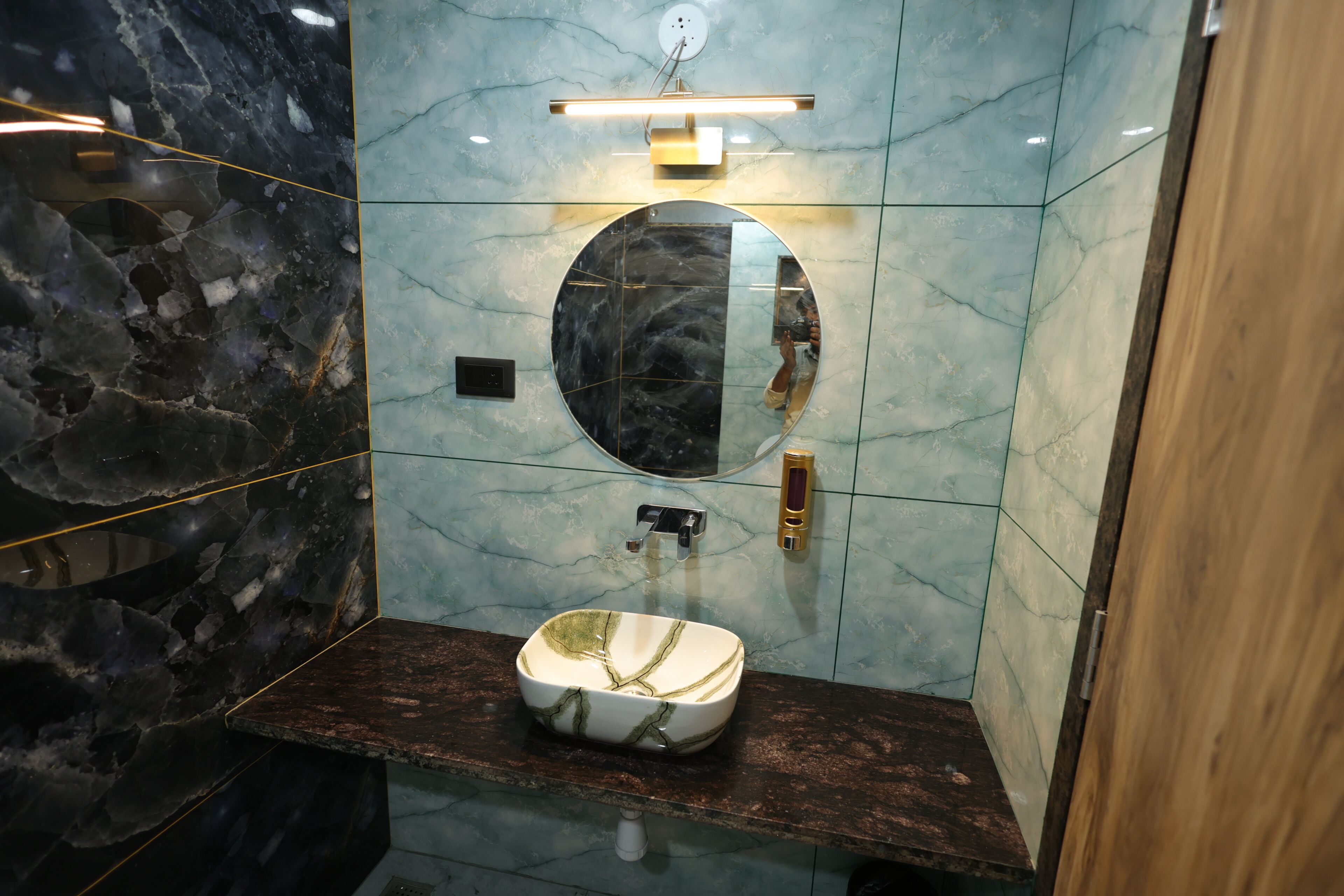 A bathroom with a marble vanity, a round mirror, a wall-mounted light, and a modern faucet.