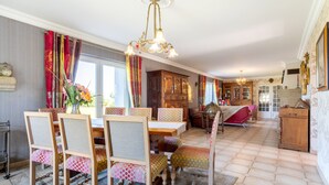 A dining area with a wooden table, chairs, and a chandelier. There is a cabinet and a sofa in the background.