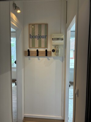 A hallway with a 'bonjour' sign, a coat rack, and a thermostat. - Seaside apartment (Saint-Aubin-sur-Mer)
