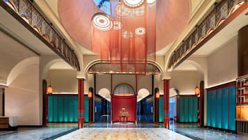 Eine geräumige Lobby mit hoher Decke, aufwendiger Deckenverzierungen und einer zentral gelegenen roten Sitzecke.