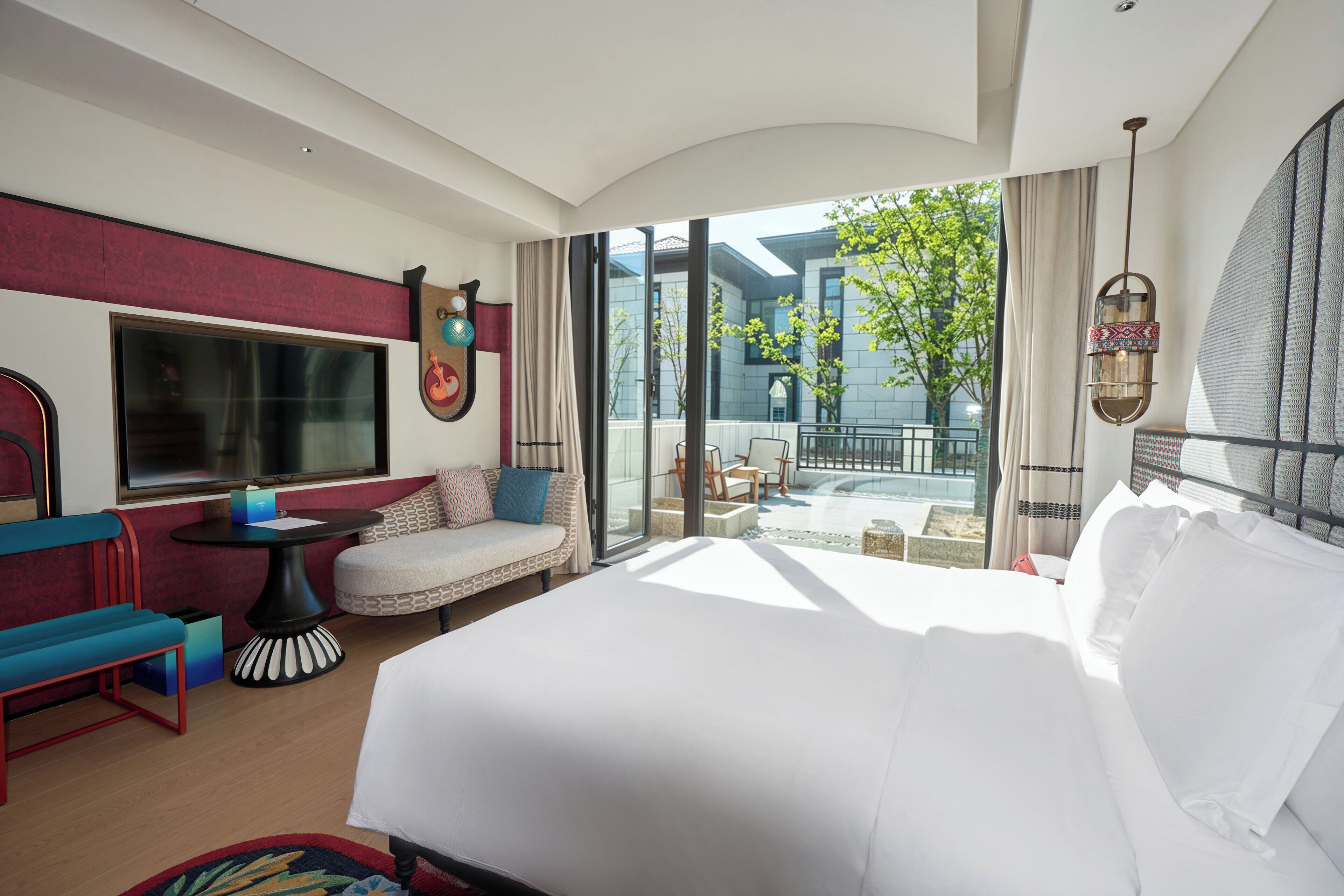 A hotel room with a large bed, a seating area with a table, and a view of the outside.