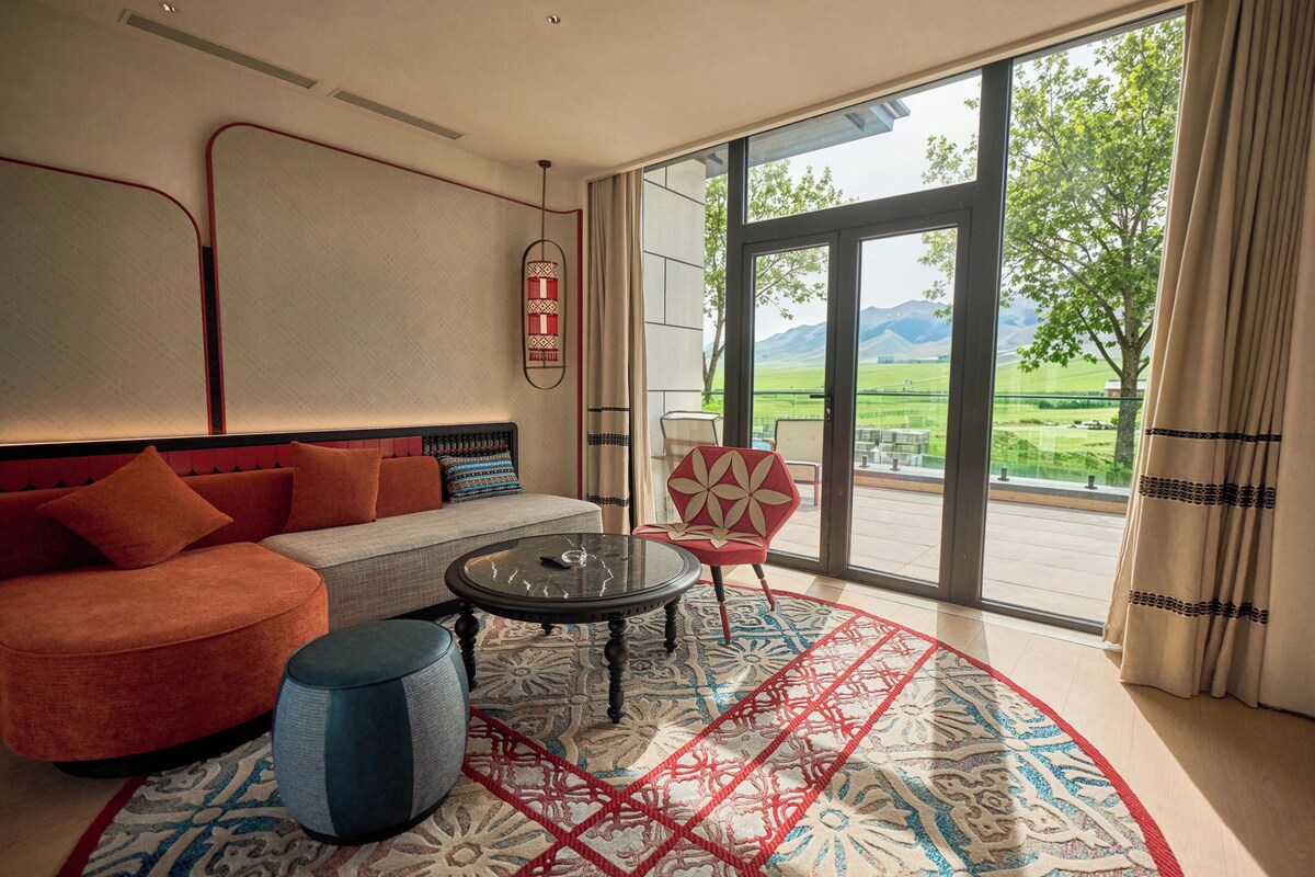 Una sala de estar moderna con un sofá, una mesa de centro, una alfombra estampada y un ventanal con vistas a la vegetación.