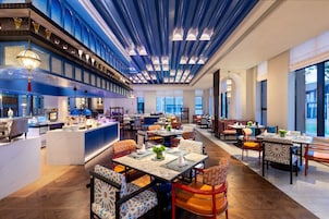 A modern restaurant with a high ceiling, multiple dining areas, and a bar.
