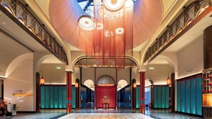En rummelig lobby med et centralt siddeområde, højt til loftet med dekorativ belysning, og udsigt til himlen gennem vinduerne.