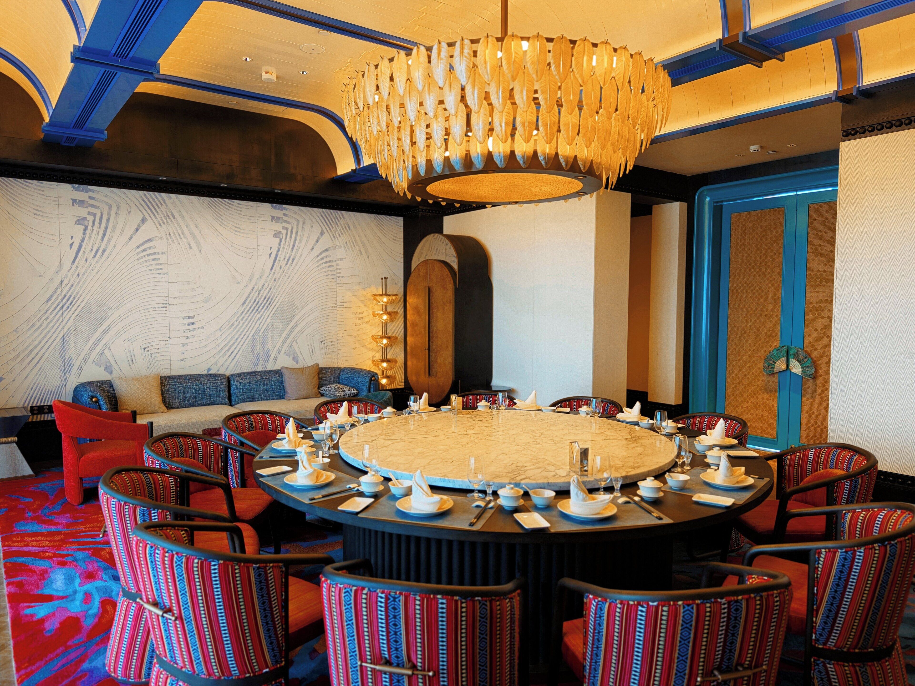 Une table ronde entourée de chaises, un canapé et un grand lustre dans une pièce aux murs à motifs et aux accents bleus.