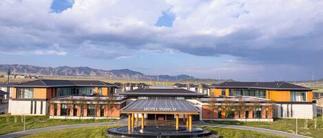 A modern hotel with a prominent entrance, solar panels, and a view of wind turbines in the background.