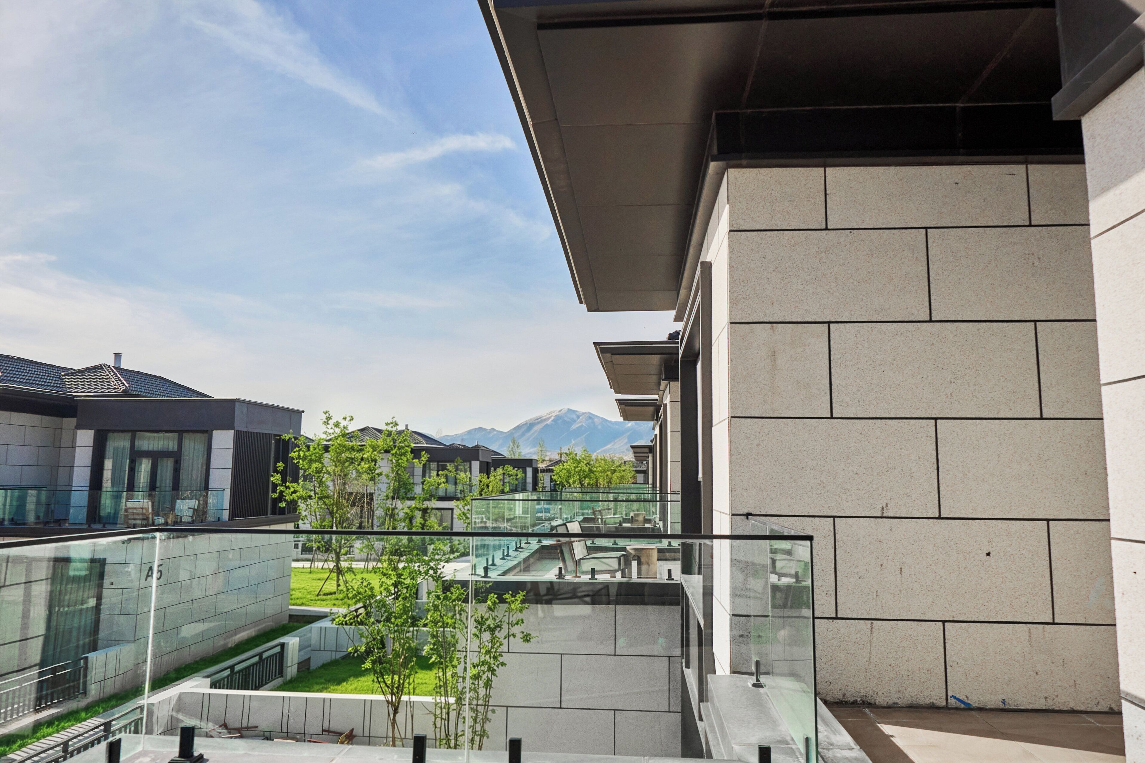 A modern building with a glass facade, a courtyard with greenery, and a view of mountains in the background.