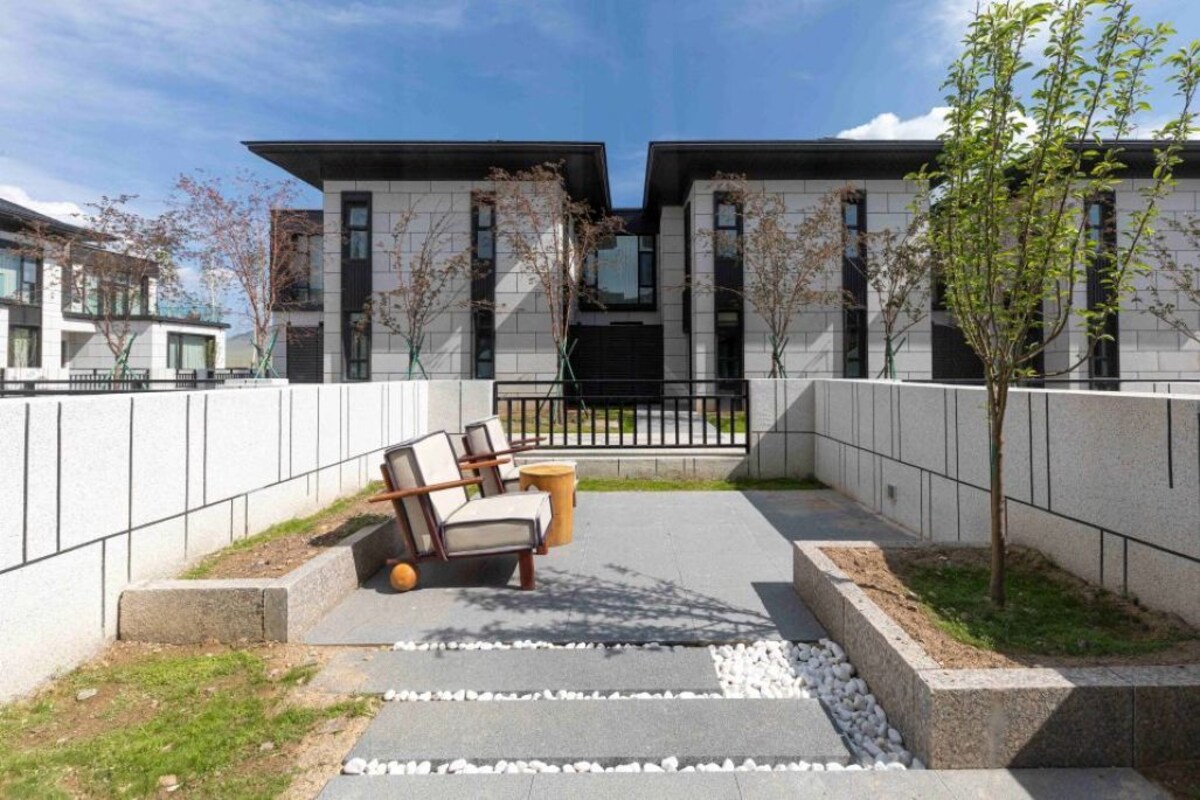 A modern building with a flat roof, large windows, and a paved courtyard with outdoor furniture.