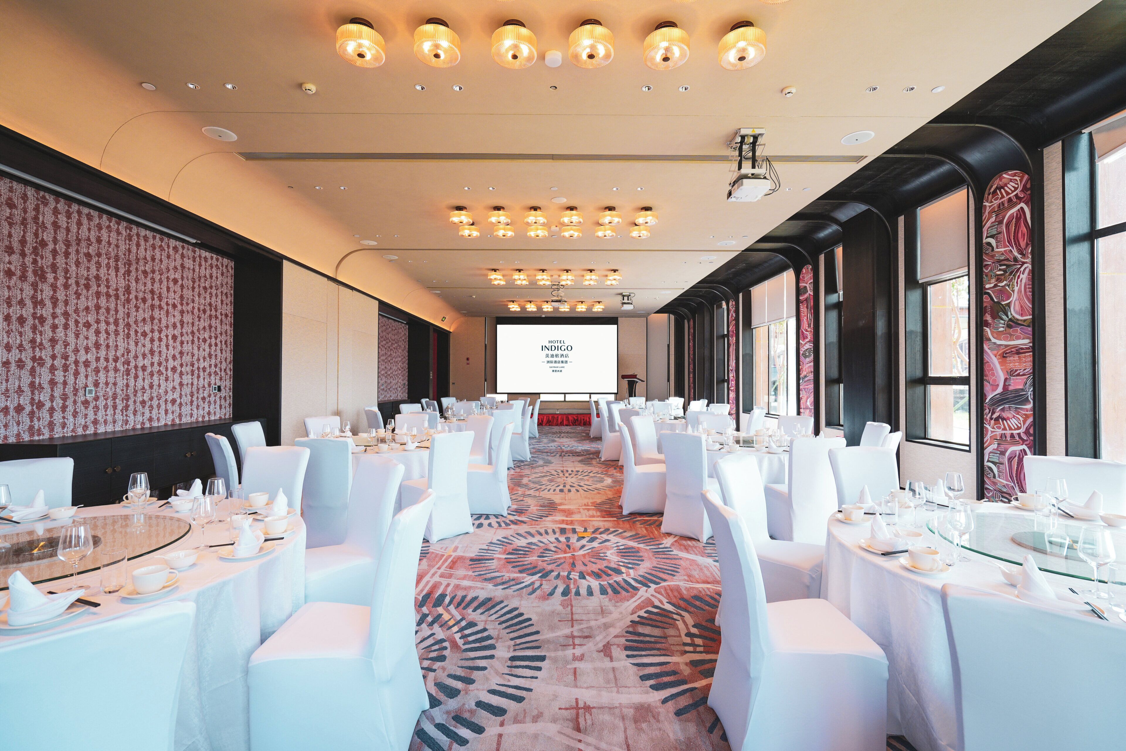 A conference room with round tables, white chairs, and a large screen at the front.