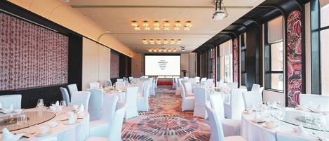 A conference room with round tables, white chairs, and a large screen at the front.