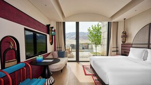 Et hotelværelse med seng, sofa, lille bord, bænk og udsigt til det fri.