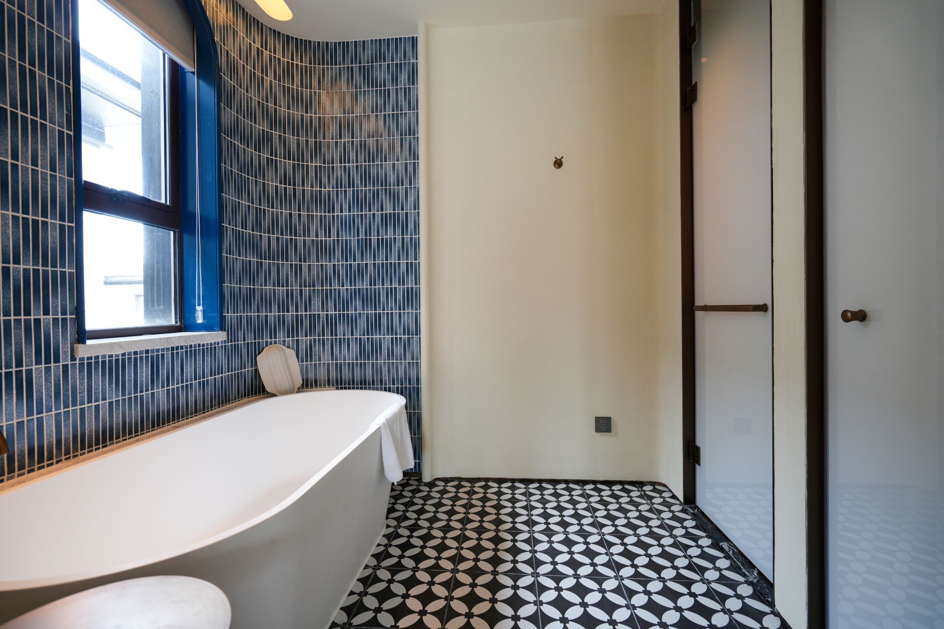 A bathroom with a white bathtub, a window, and a patterned floor.