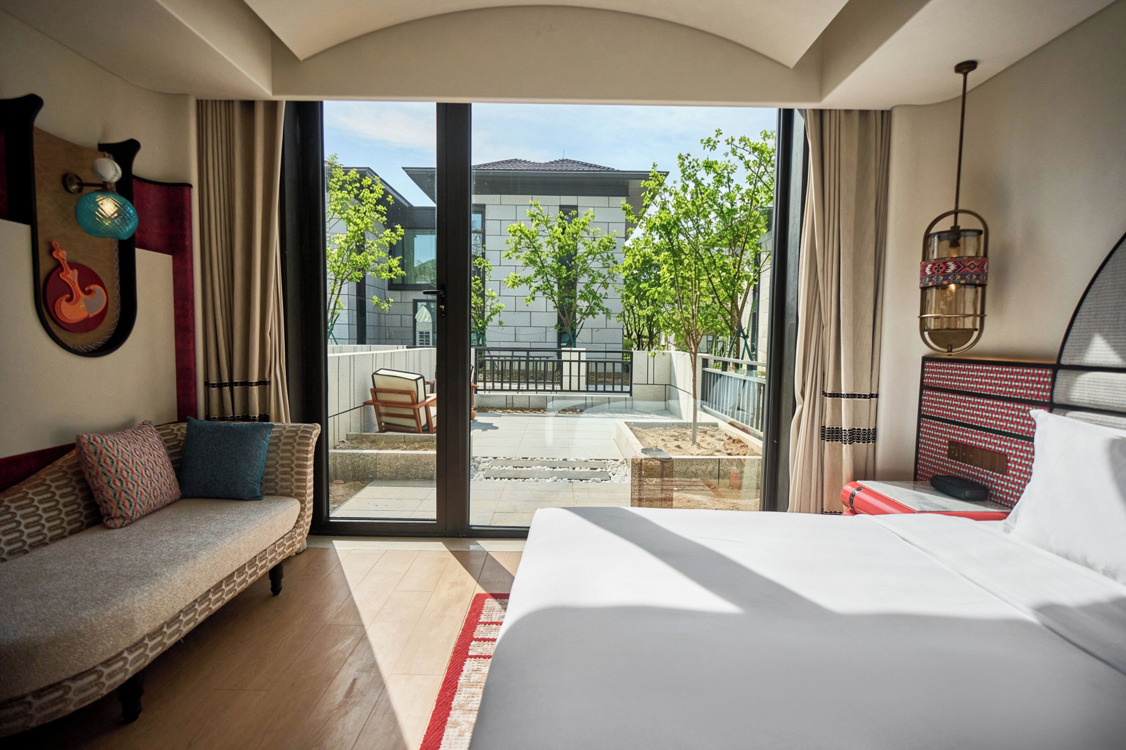 A hotel room with a bed, a sofa, a balcony with a view of the outside, and a dining area.