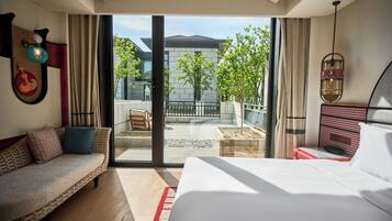 A hotel room with a bed, a sofa, a balcony with a view of the outside, and a dining area.