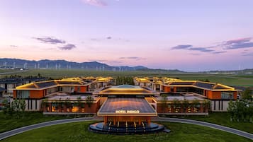 Un hotel amb un edifici central anomenat 'HOTEL INDIGO', envoltat d'edificis moderns, amb un fons de molins de vent i un paisatge amb turons.