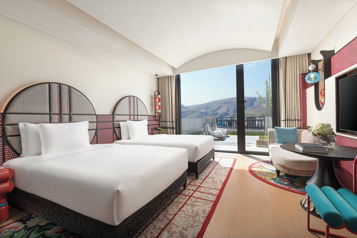 Habitación de hotel con una cama grande, un sofá, una mesita y vistas al exterior.
